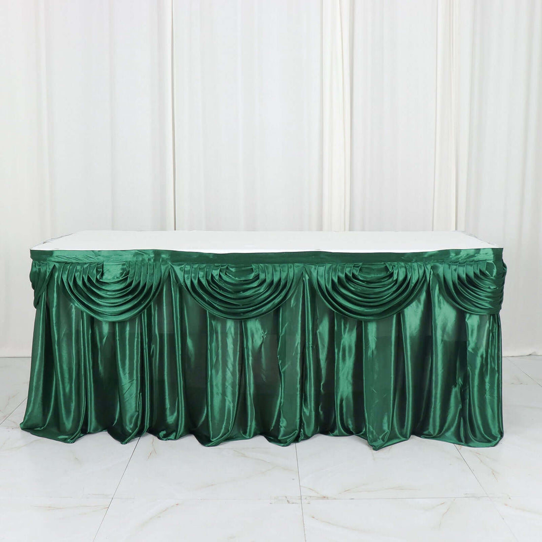 Green satin table skirt with elegant draping for events and celebrations.