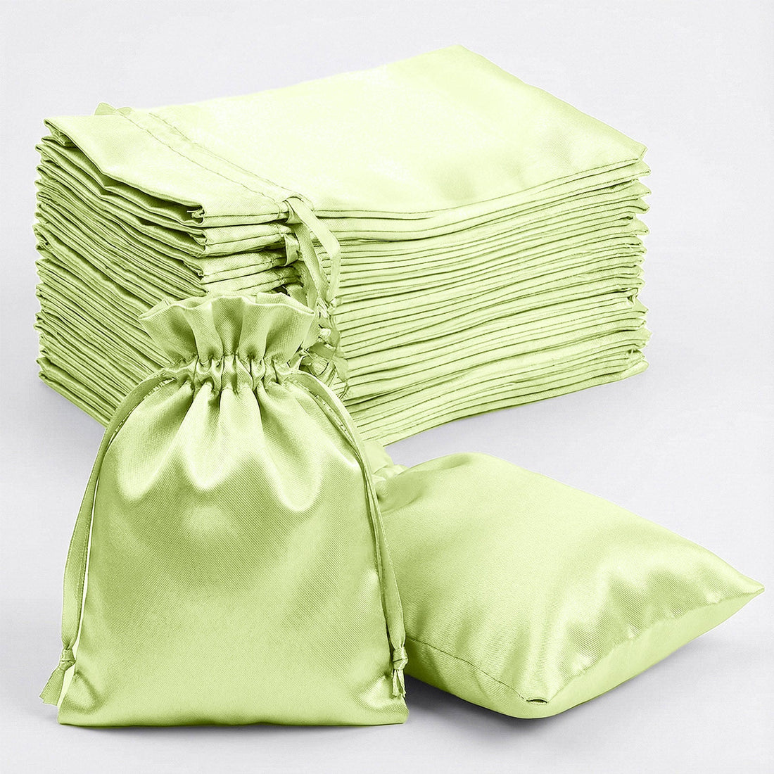 Green satin drawstring bags stacked with one bag and pillow on white background.