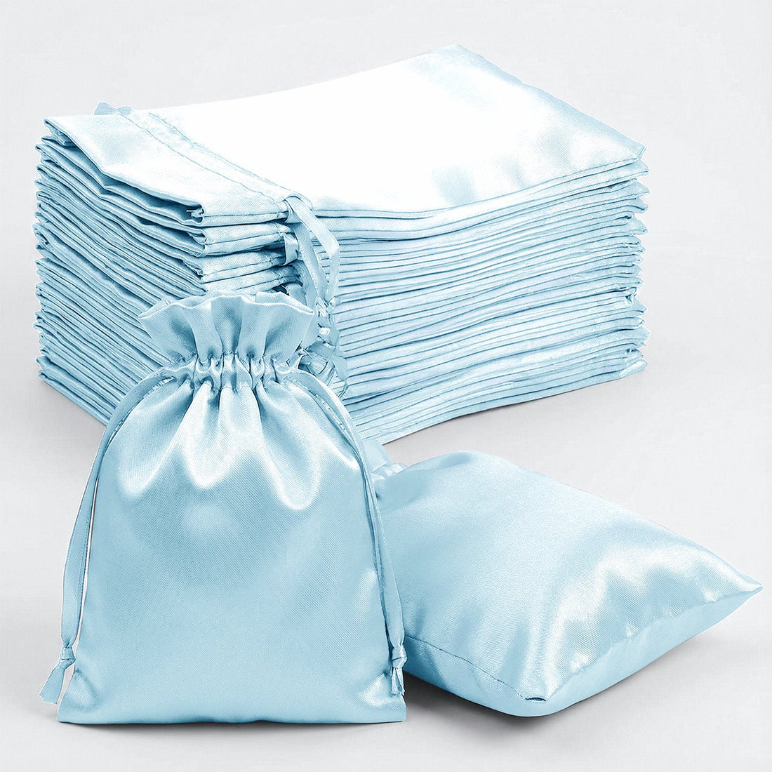Stack of light blue satin bags and flat fabric sheets on a white background.