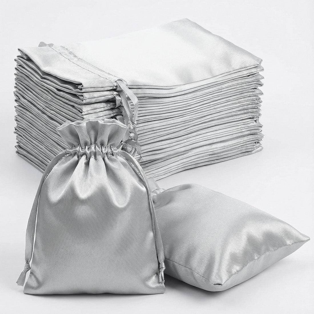 Silver satin drawstring bags and flat pouches stacked on white background.