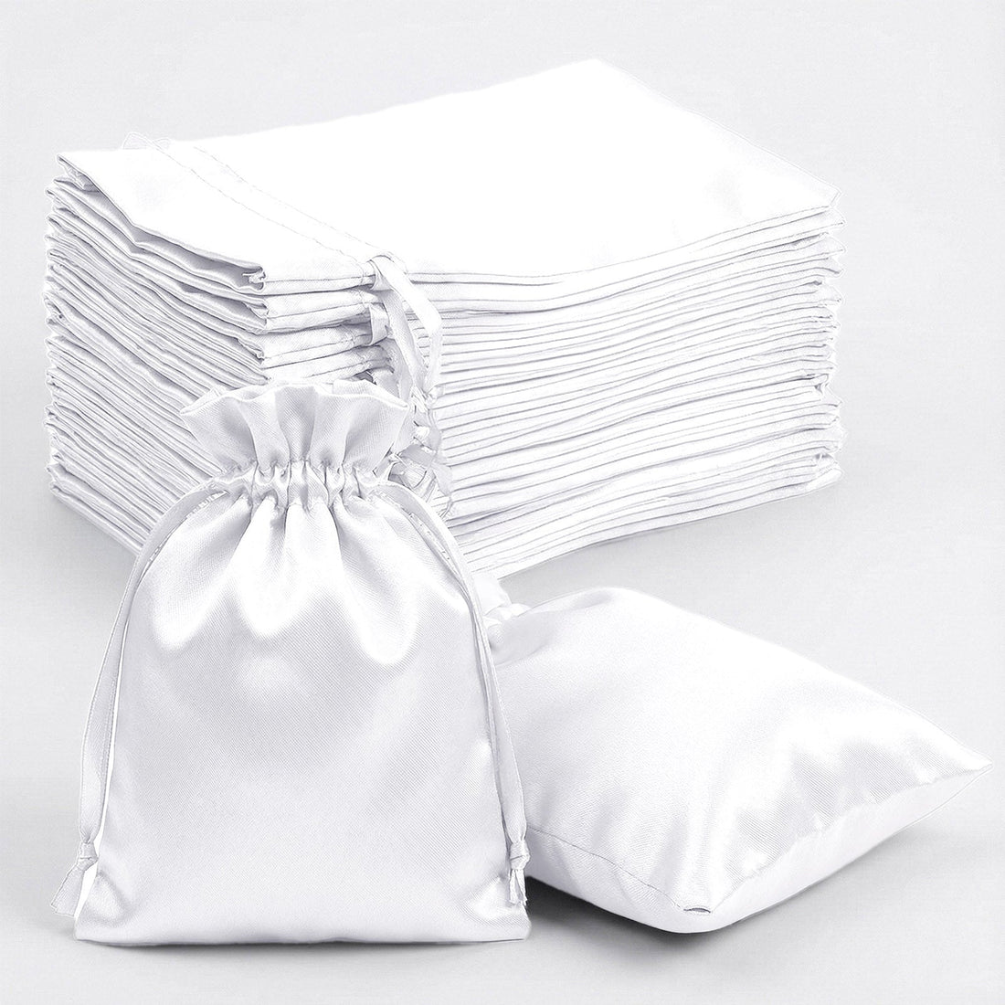 White satin drawstring bags stacked and one bag in front.