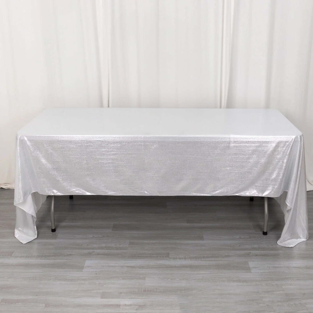 Silver tablecloth draped over a table on a wooden floor.