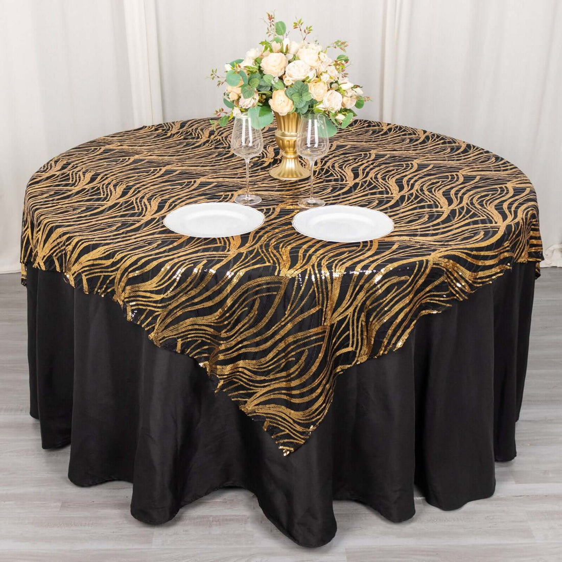 Elegant black and gold tablecloth draped over round table with floral centerpiece.