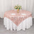 Rose gold patterned table overlay on a round white table with floral centerpiece.