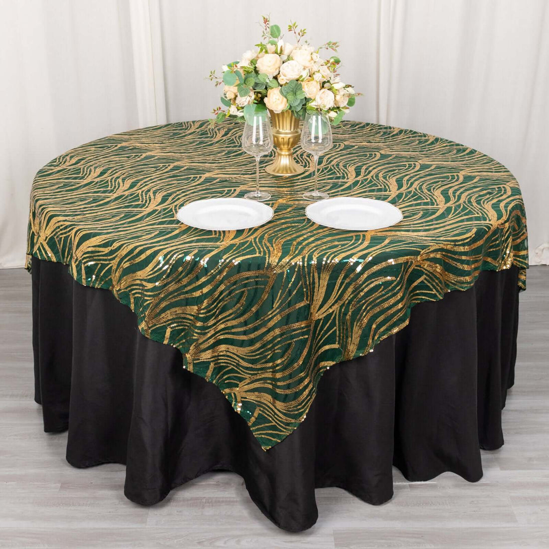 Elegant green and gold wave patterned tablecloth on a round table with floral centerpiece.