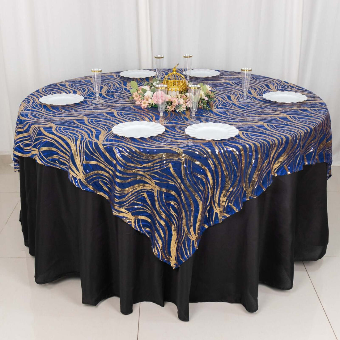 Elegant blue and gold patterned tablecloth on a round table with white plates.