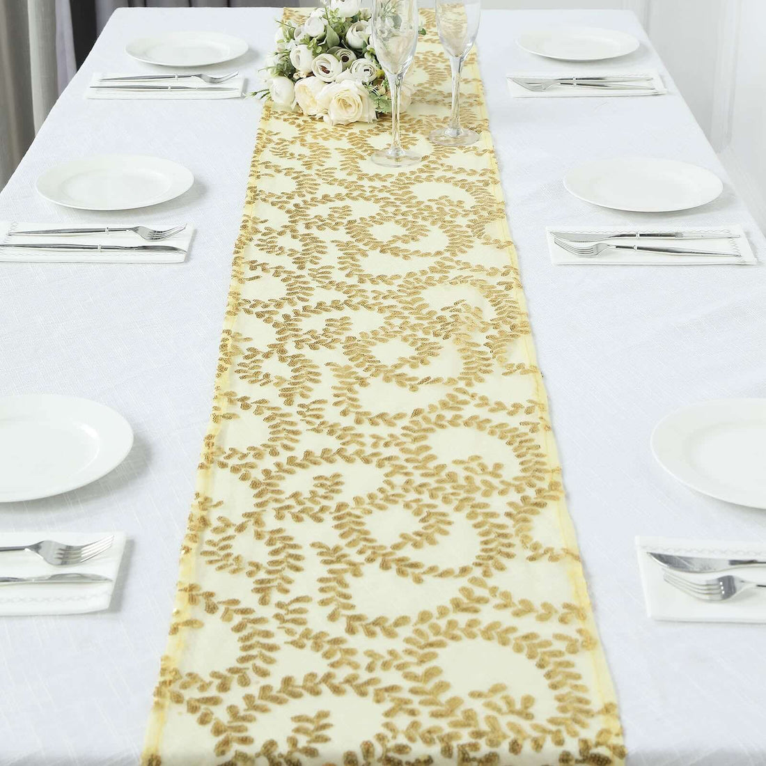 Elegant gold leaf table runner on a white table setting with plates and glasses.