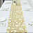 Elegant gold leaf table runner on a white table setting with plates and glasses.