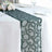 Embroidered green table runner on a white tablecloth with floral decor.