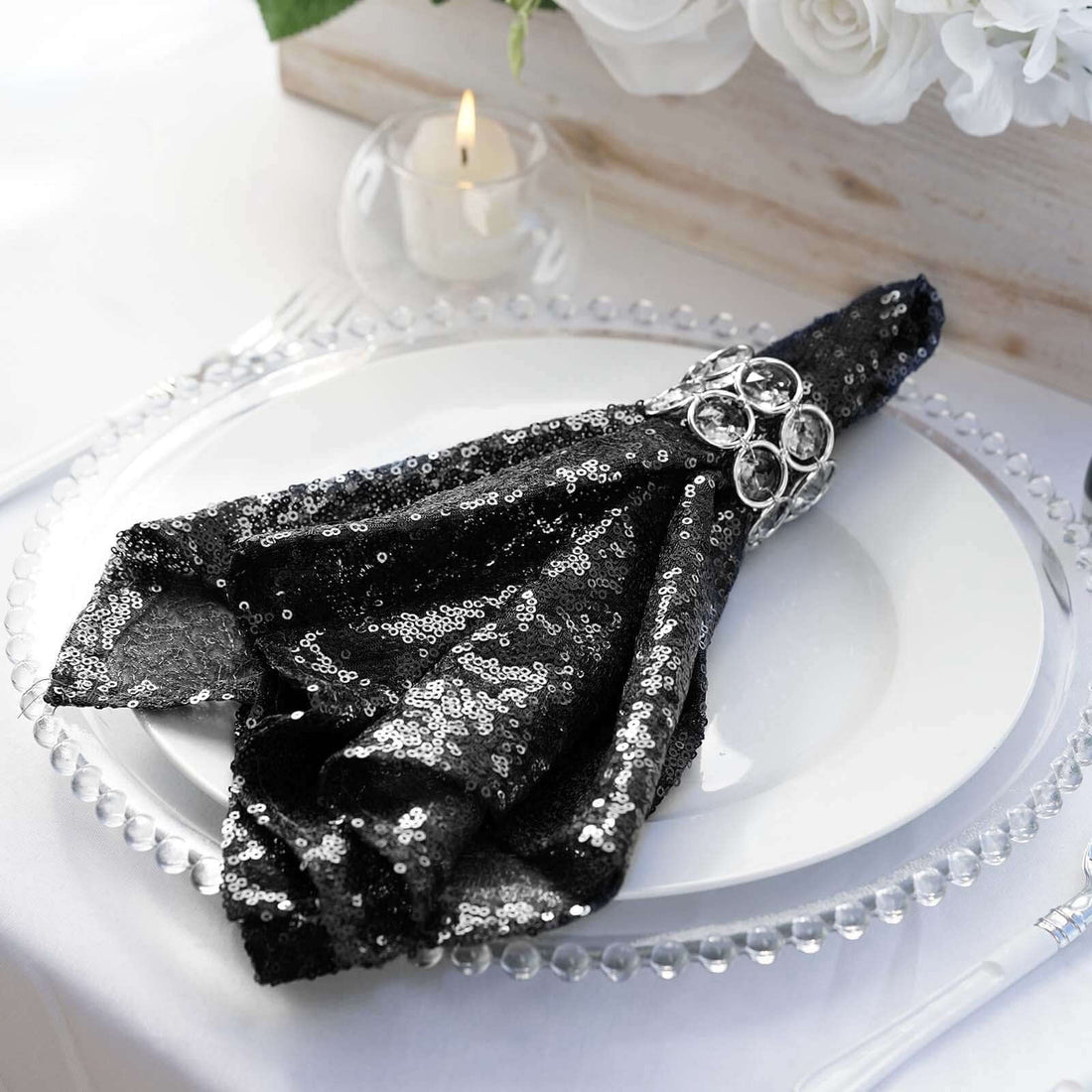 Black sequin napkin elegantly draped on a white plate with a decorative ring.