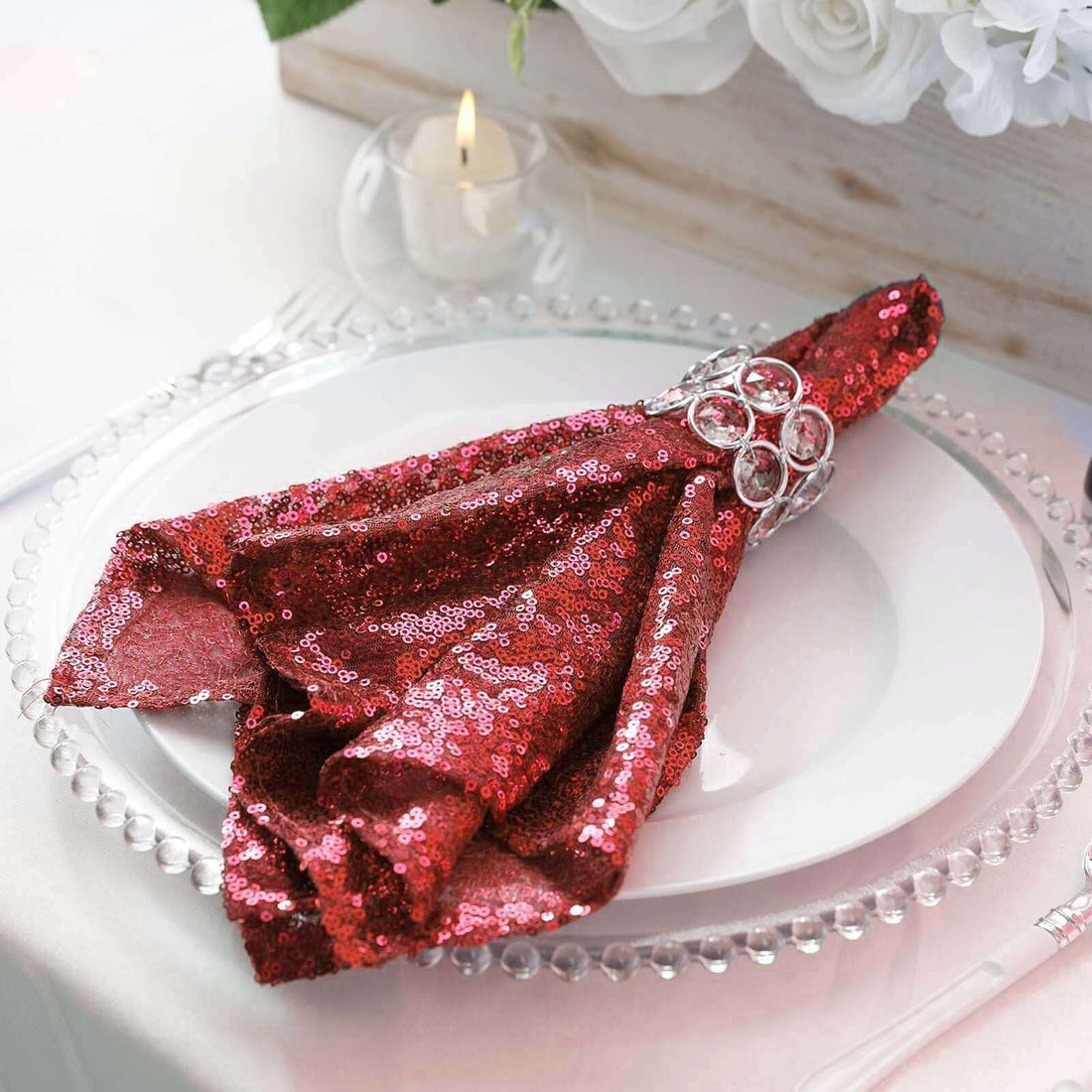 Red sequin napkin elegantly folded on a white plate with a decorative ring.