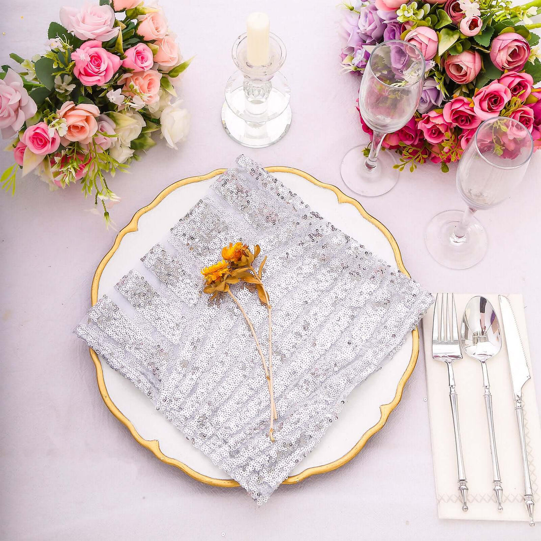 Elegant table setting with silver napkin, candle, and floral arrangements.