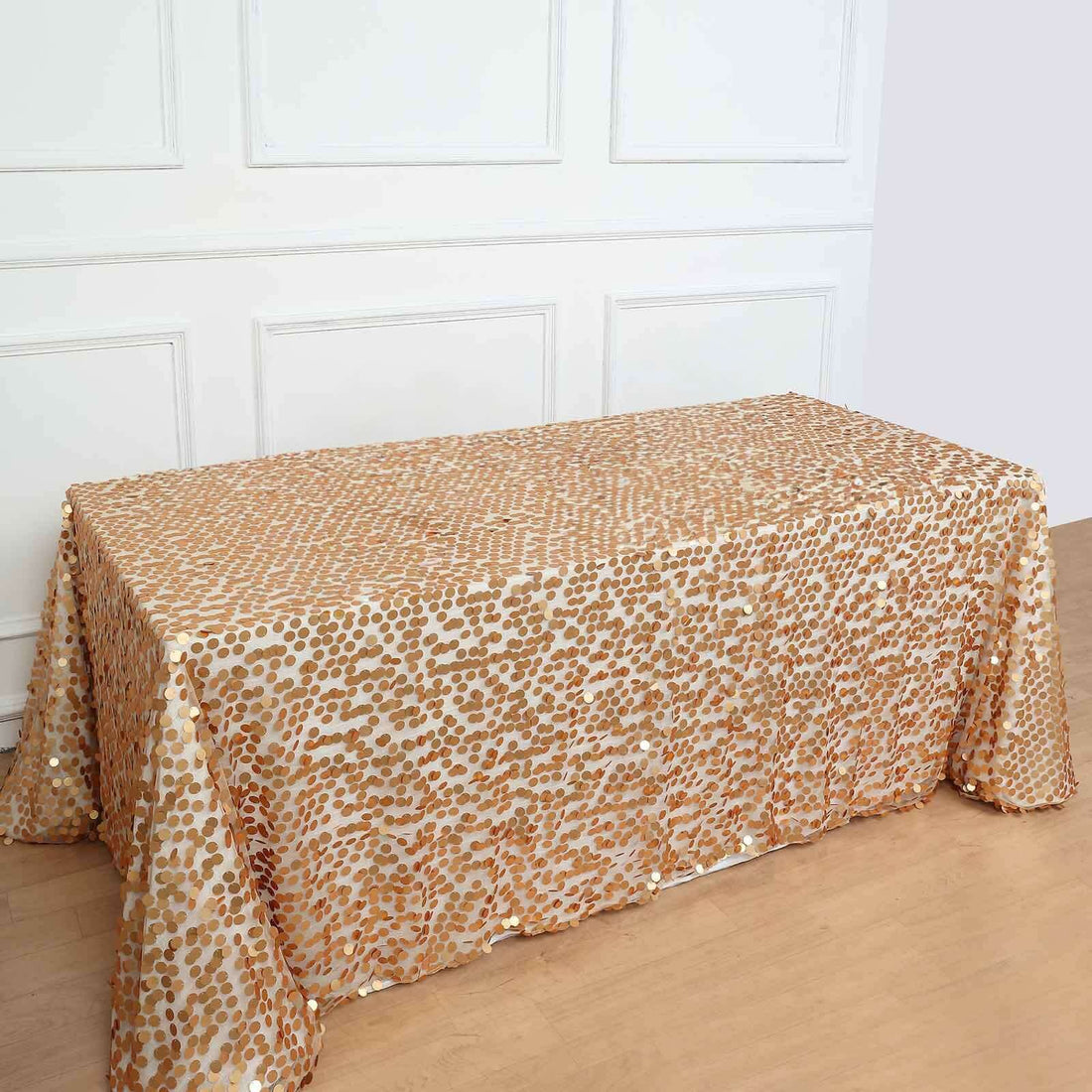 Gold sequin tablecloth on a wooden table against a white wall background.