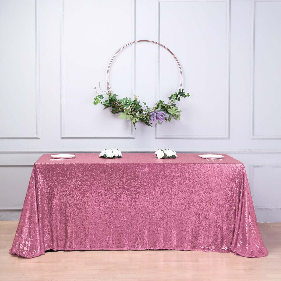 Pink sequin tablecloth draped over a table with floral centerpiece and greenery.