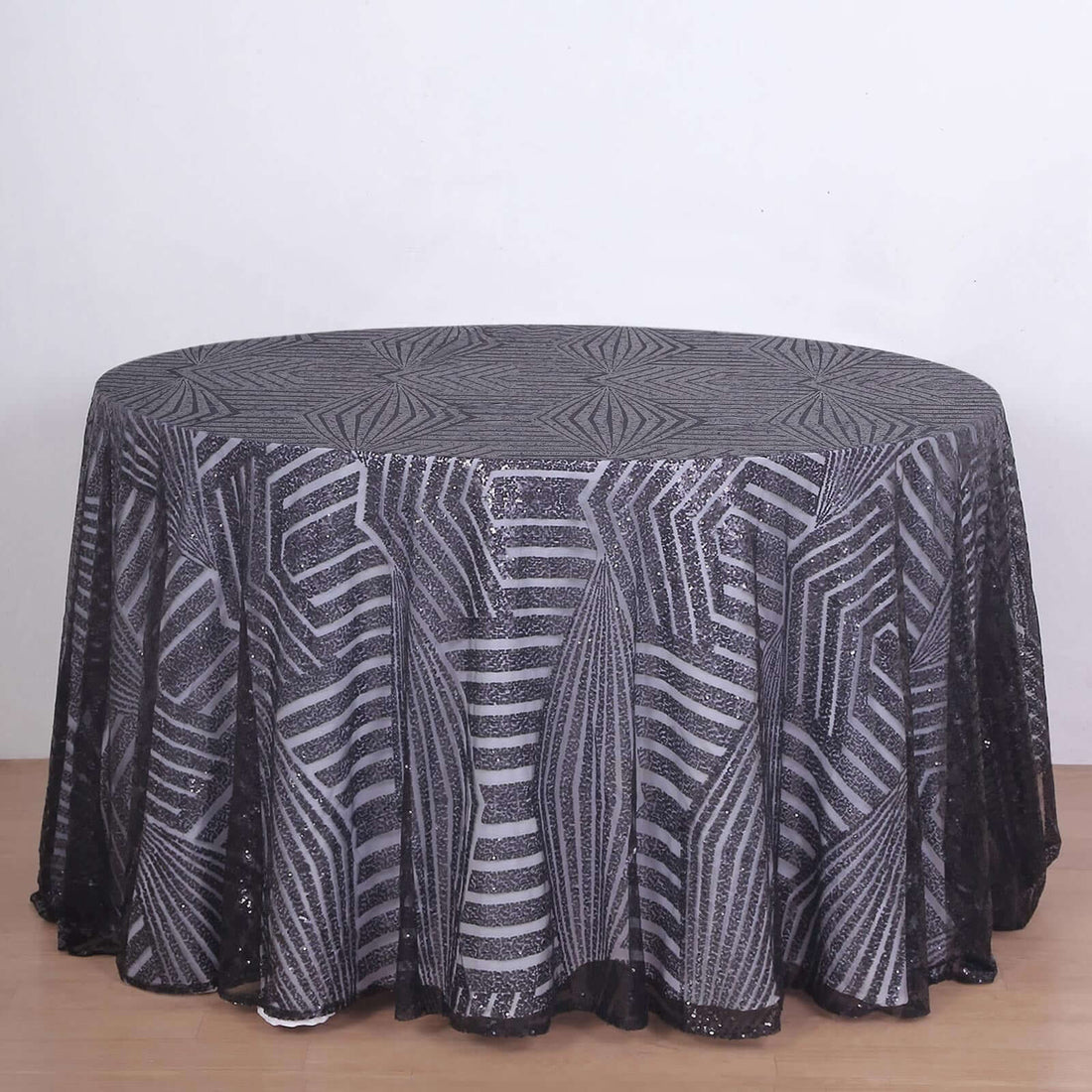 Round black and silver patterned tablecloth on a wooden surface.
