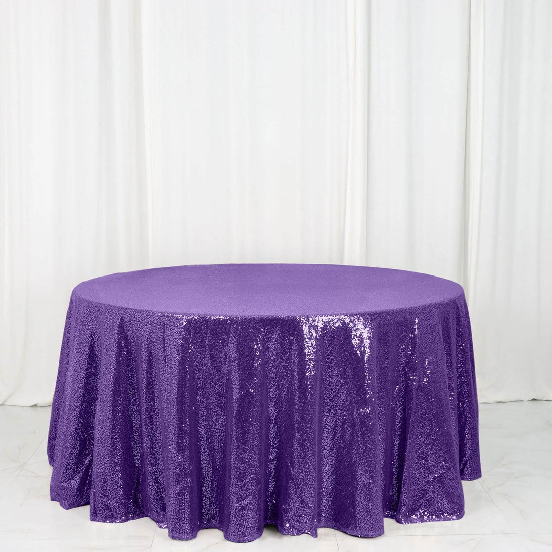 Purple sequin tablecloth on a round table against a white backdrop.
