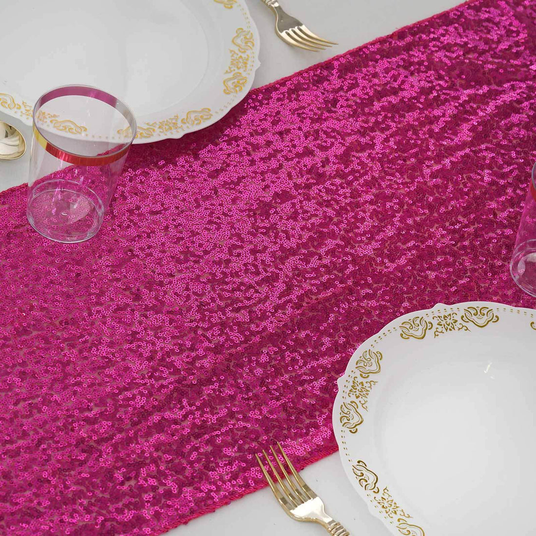 Pink sequin table runner with white plates and glassware on a table.