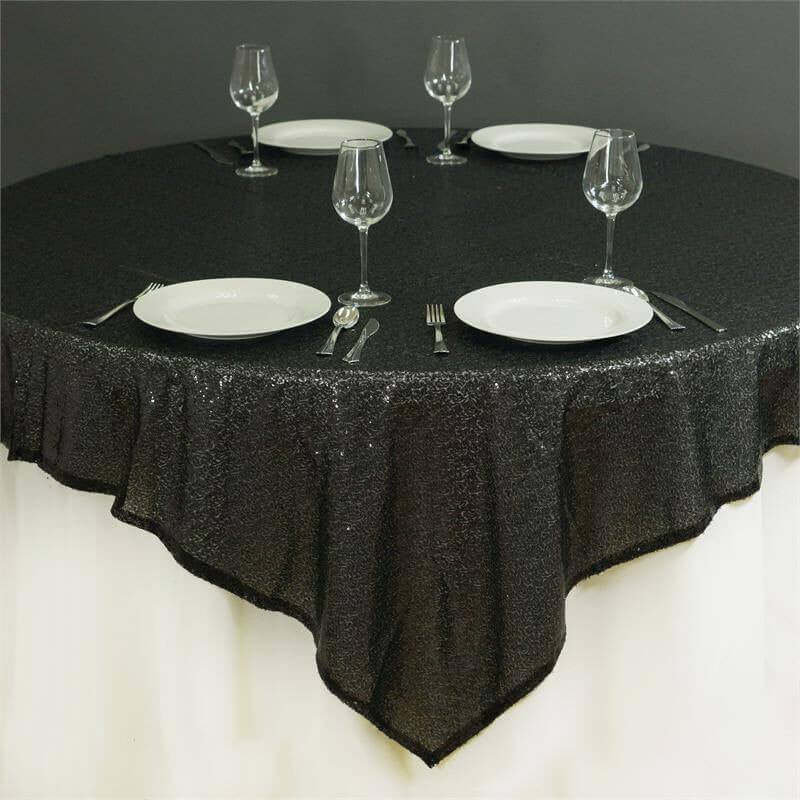 Black tablecloth on a round table set with plates and glassware.