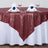 Red sequin tablecloth draped over a round table set with dinnerware and napkins.