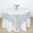 Round table set with a decorative silver lace tablecloth and floral centerpiece.