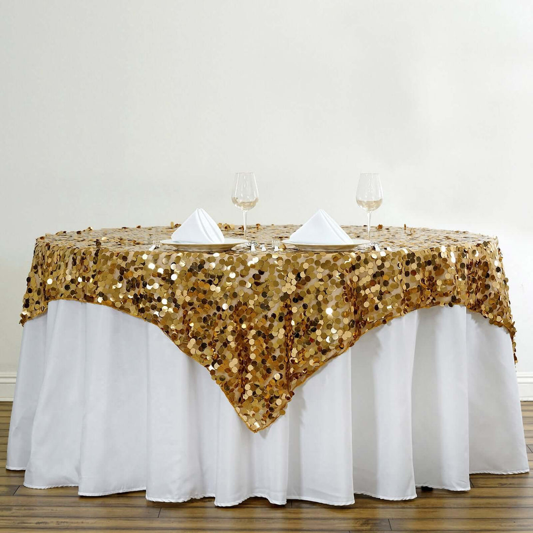 Gold sequin tablecloth draped over a round table with wine glasses and napkins.