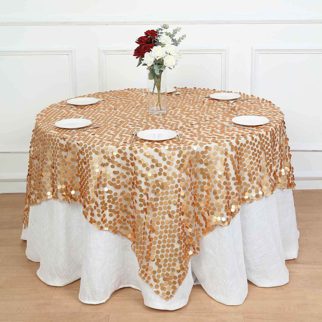 Gold polka dot tablecloth draped over a round table with white plates and flowers.