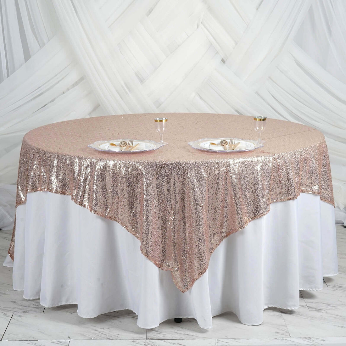 Rose gold sequin tablecloth draped elegantly on a round table with dinner plates.