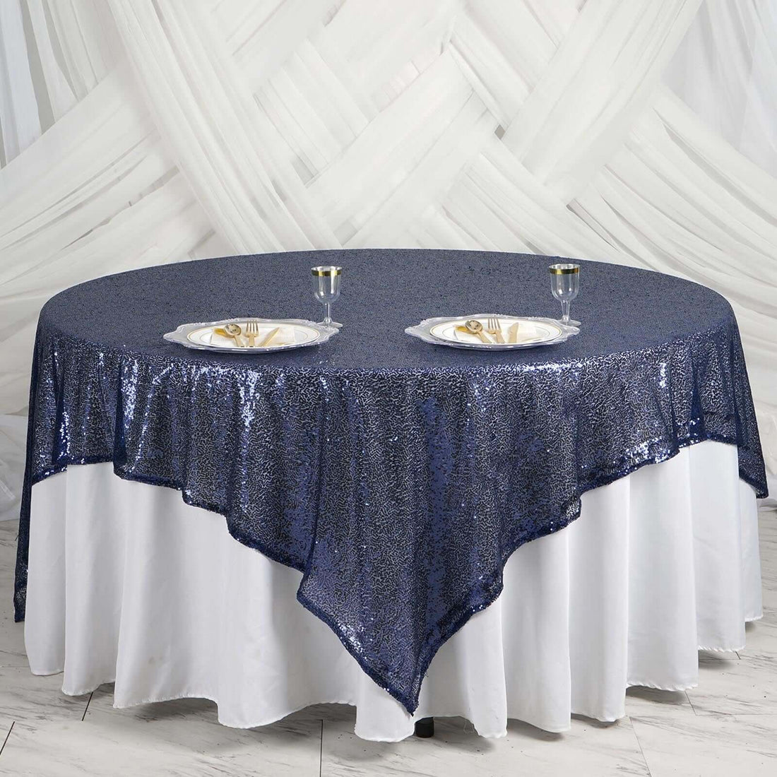 Navy sequin tablecloth draped over a round table with plates and glasses