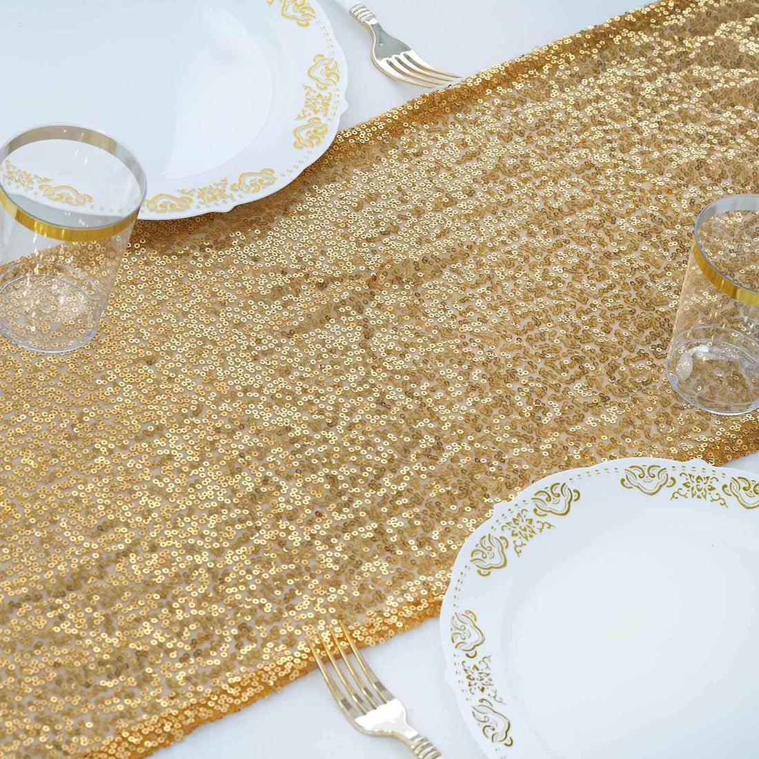 Gold sequin table runner with elegant plates and glasses for festive dining decor.