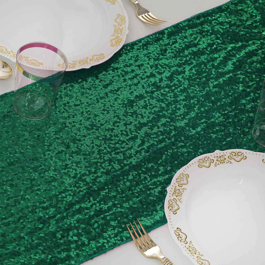 Green sequin table runner with elegant gold-trimmed plates and clear glasses.