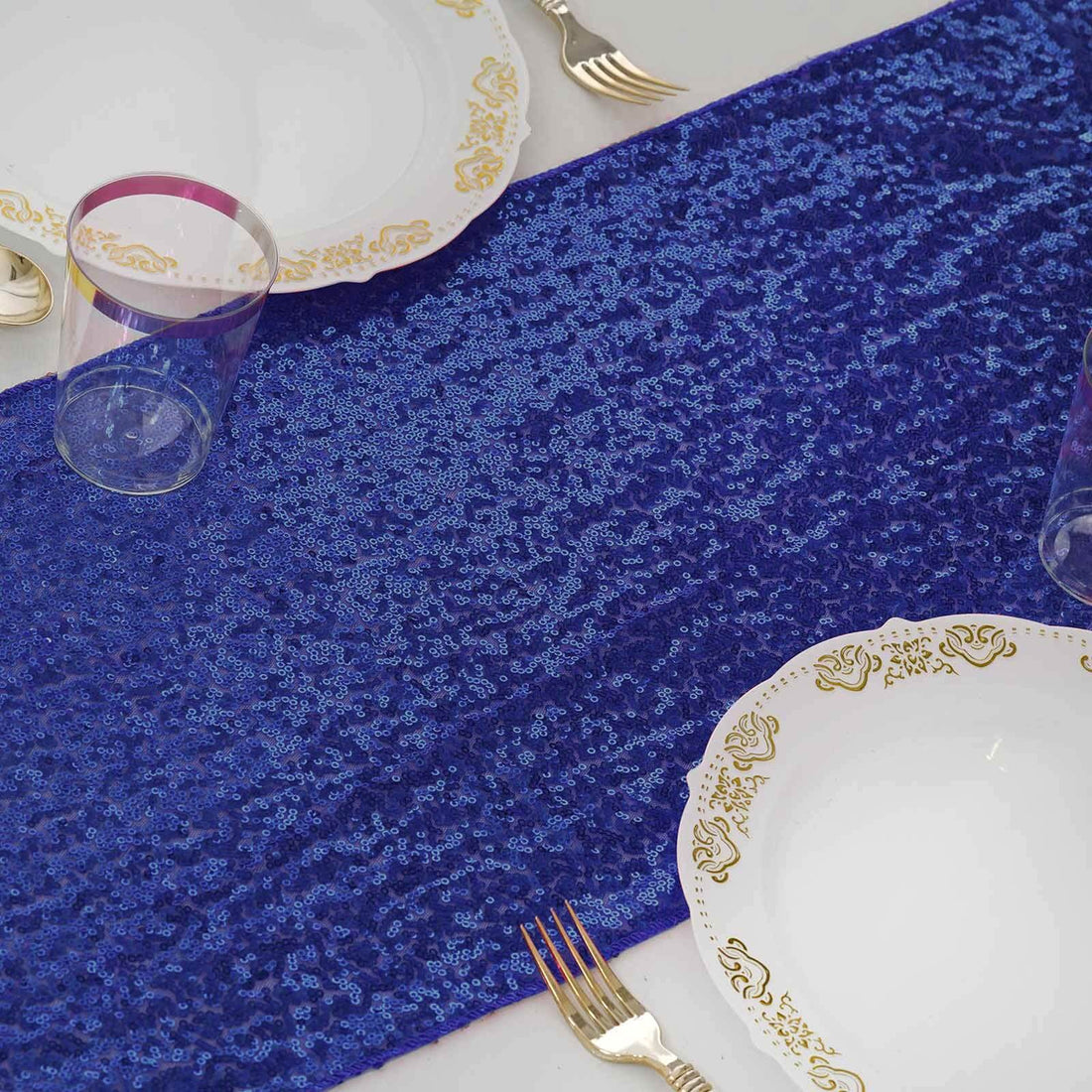 Blue sequin table runner with elegant plates and glassware set for dining.