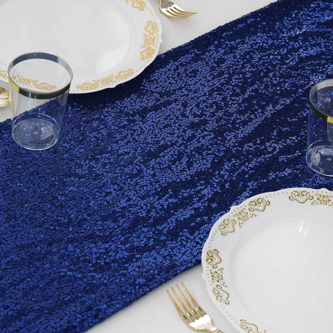 Navy sequin table runner with elegant plates and glasses set for dining.
