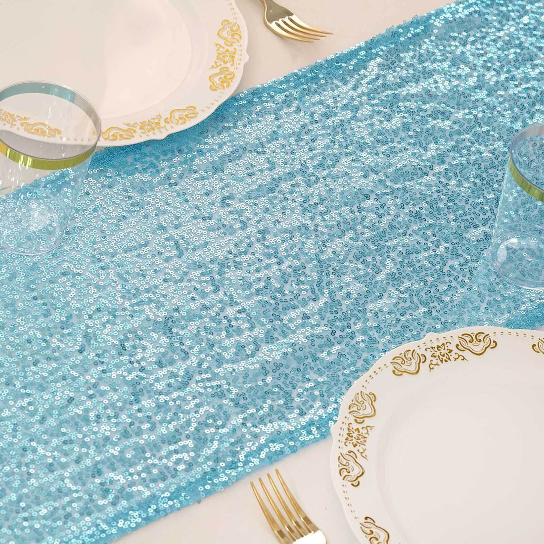 Blue sequin table runner on a dining table with elegant plates and glasses.