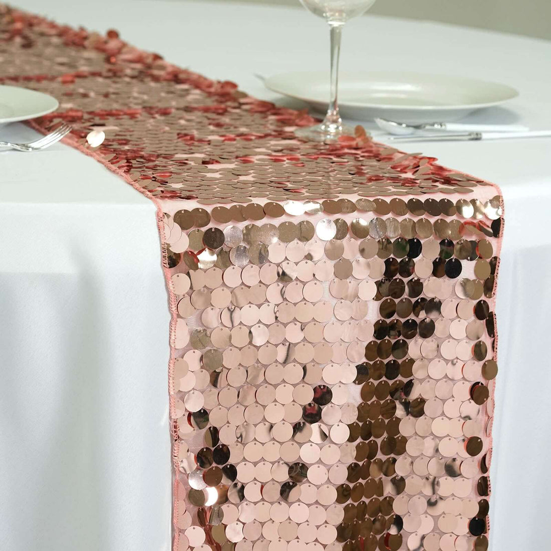 Rose gold sequin table runner on a white tablecloth.