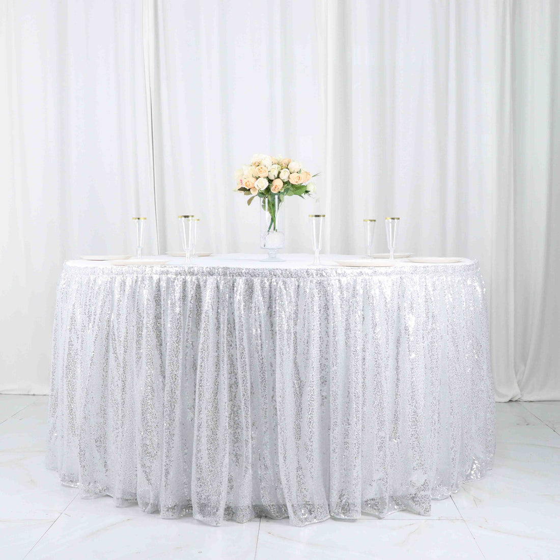 Round table with silver sequin tablecloth and floral centerpiece.