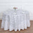 Round white tablecloth with silver floral design on a dining table.