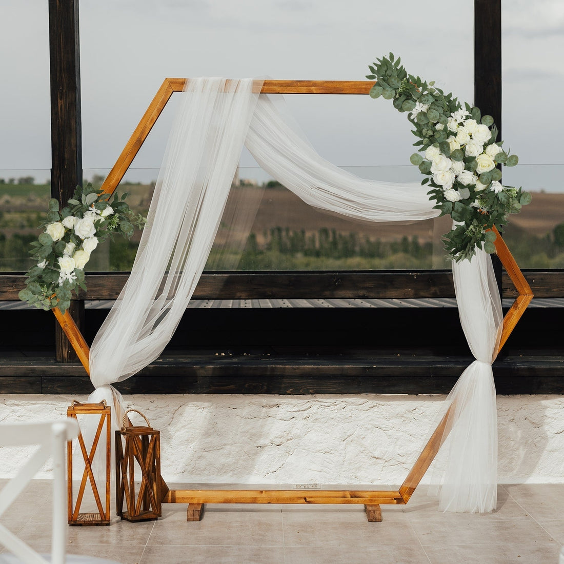 Wooden hexagon arch with white drapery and floral accents for weddings.