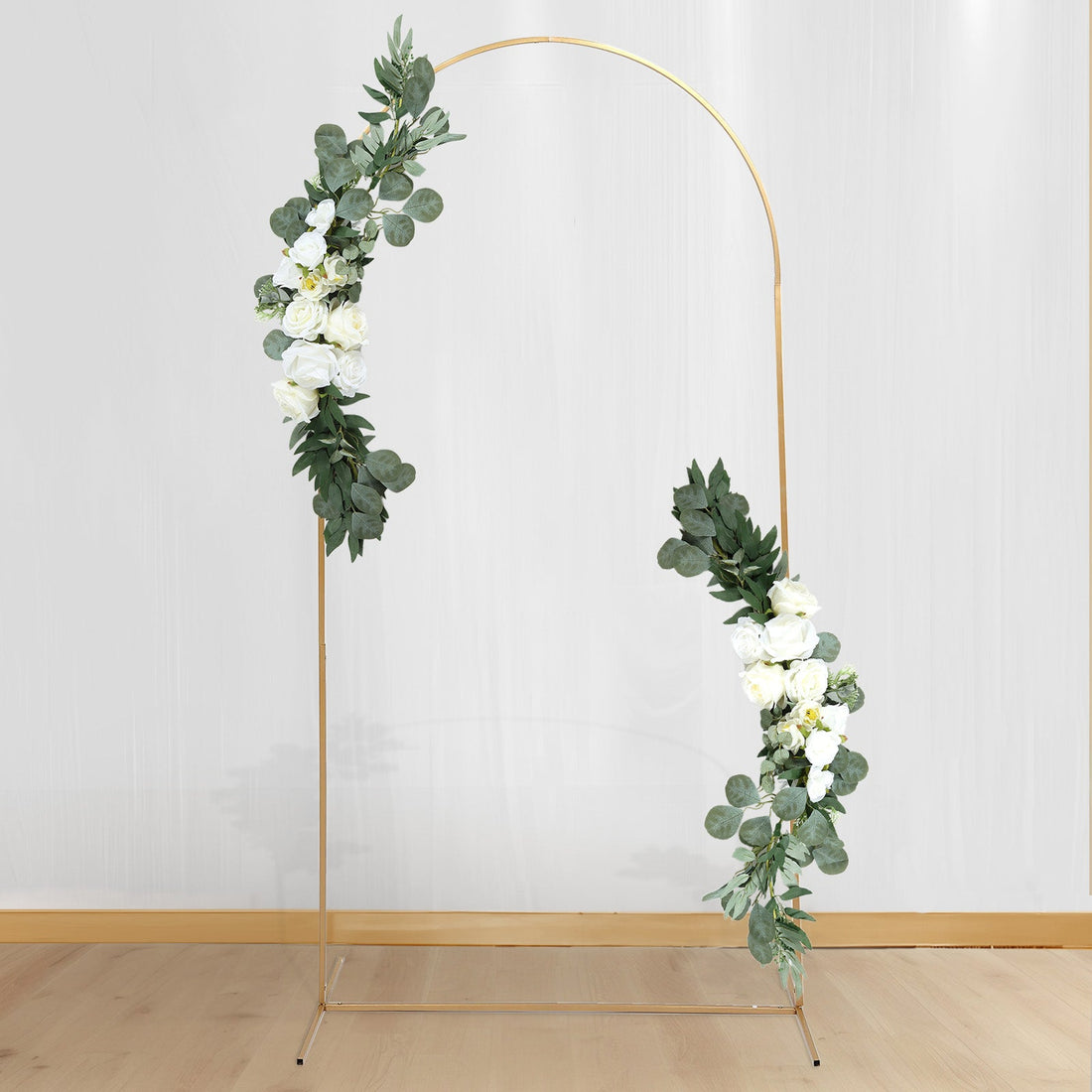 Gold floral arch with white roses and greenery on a plain backdrop.