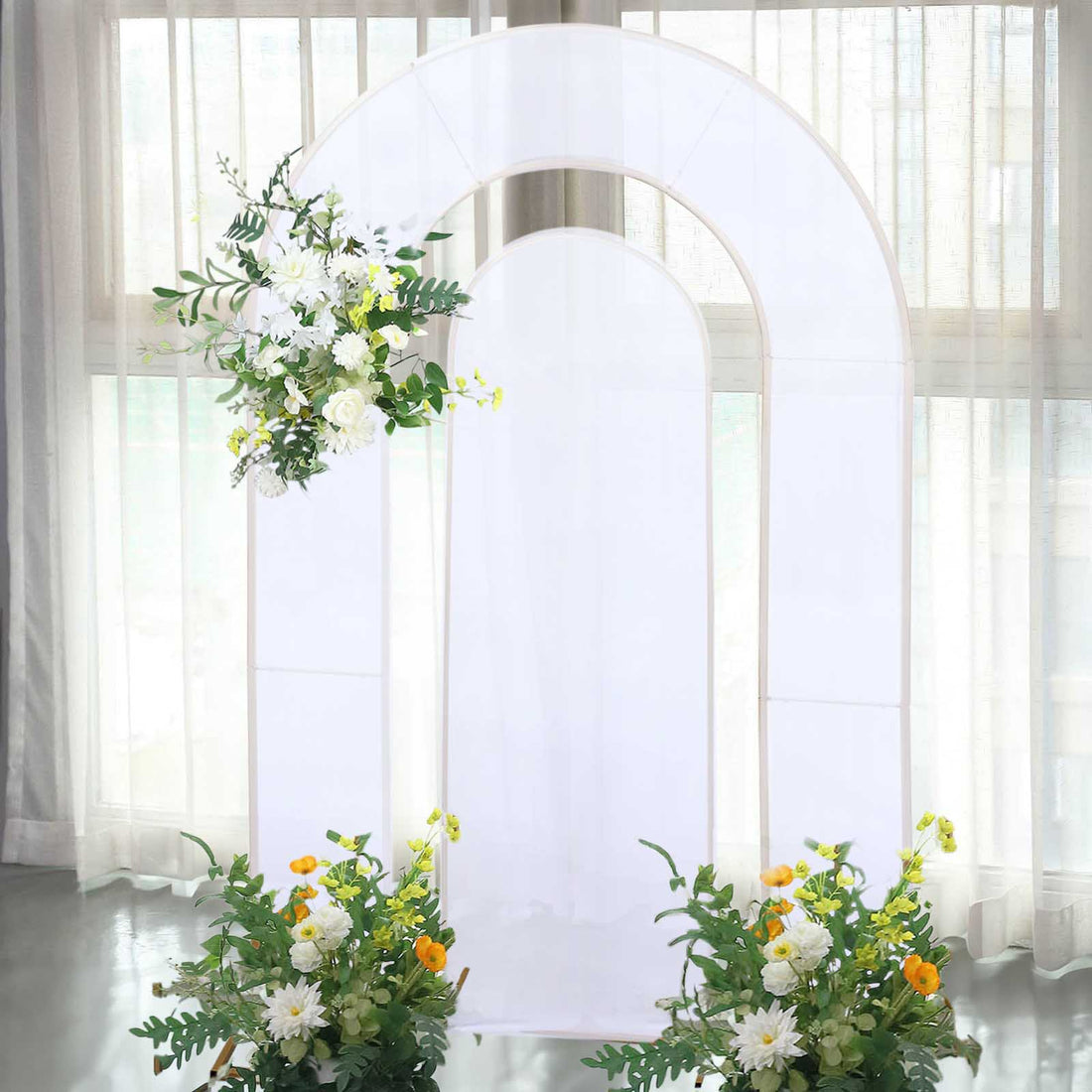 White floral arch backdrop with greenery and flowers for events or photography.