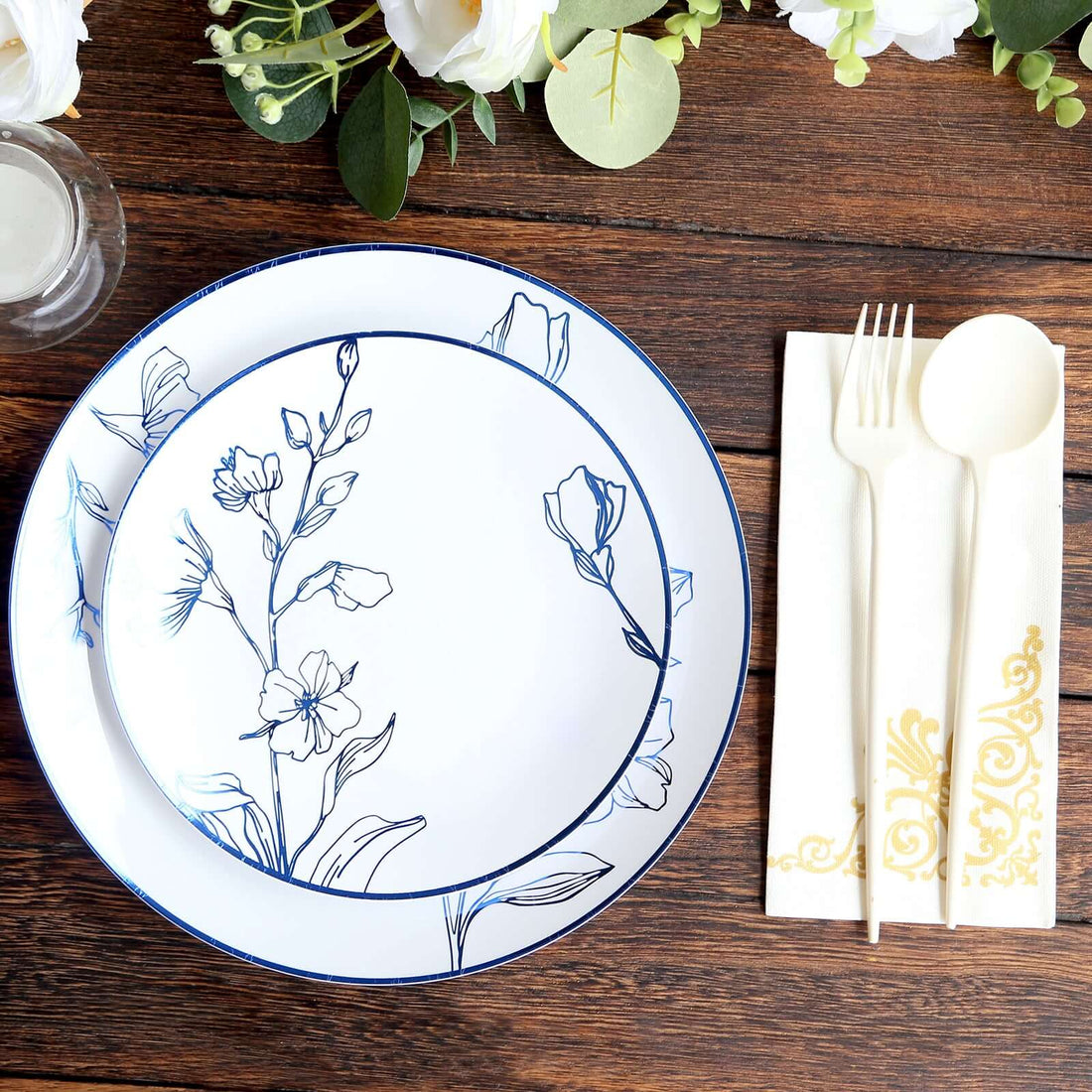 Elegant floral dinnerware set with plates, cutlery, and napkin on wooden table.
