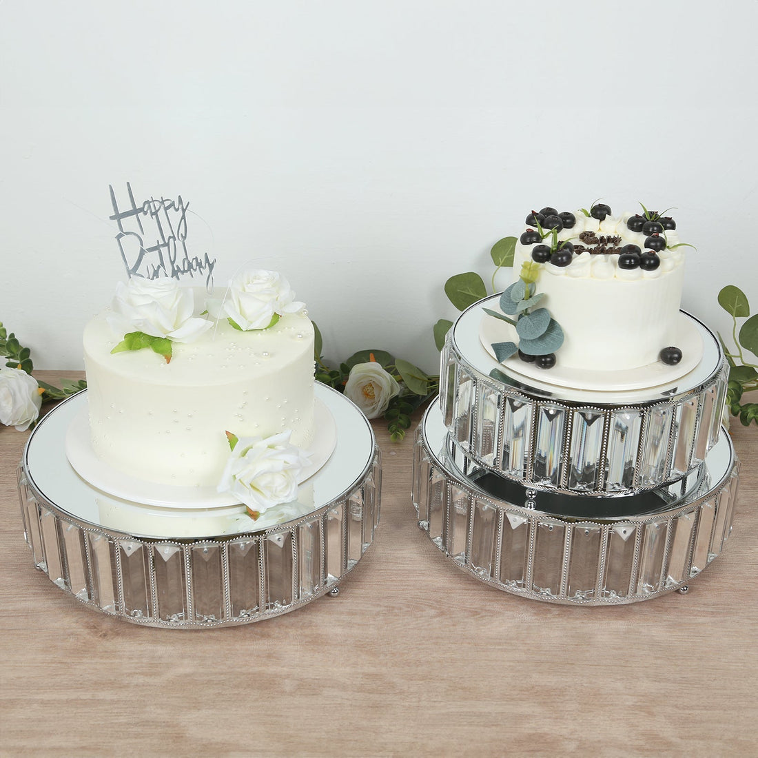 Elegant birthday cakes on mirrored stands with floral decorations.