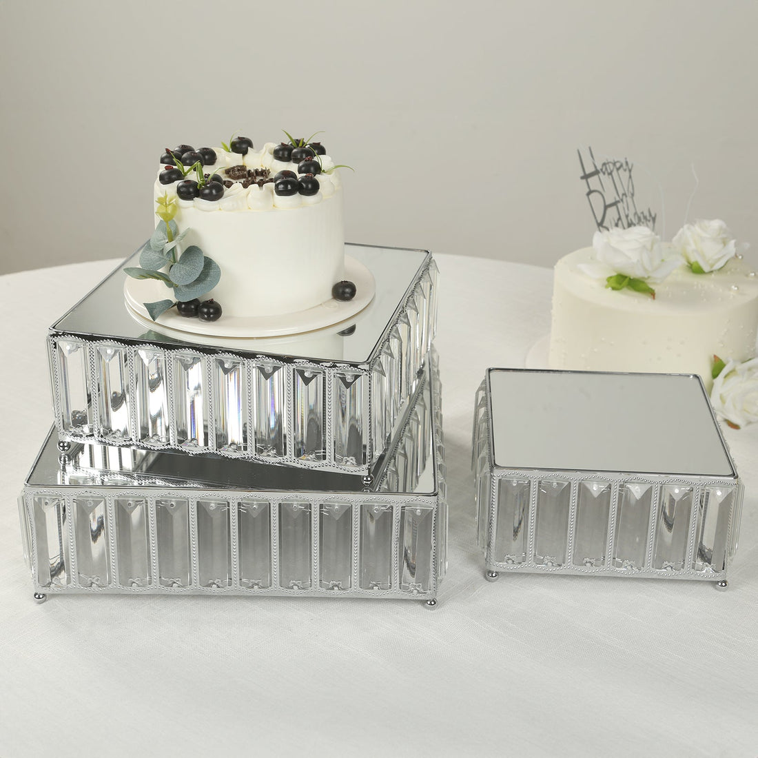Decorative mirrored cake stands stacked with cakes and flowers on a table.
