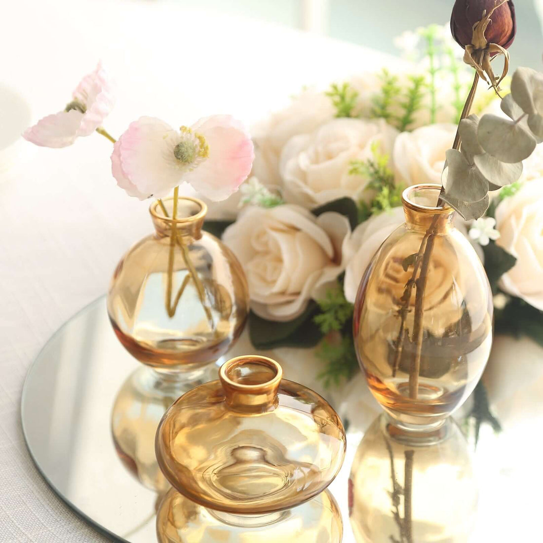 Decorative amber glass vases with flowers on a mirrored surface.