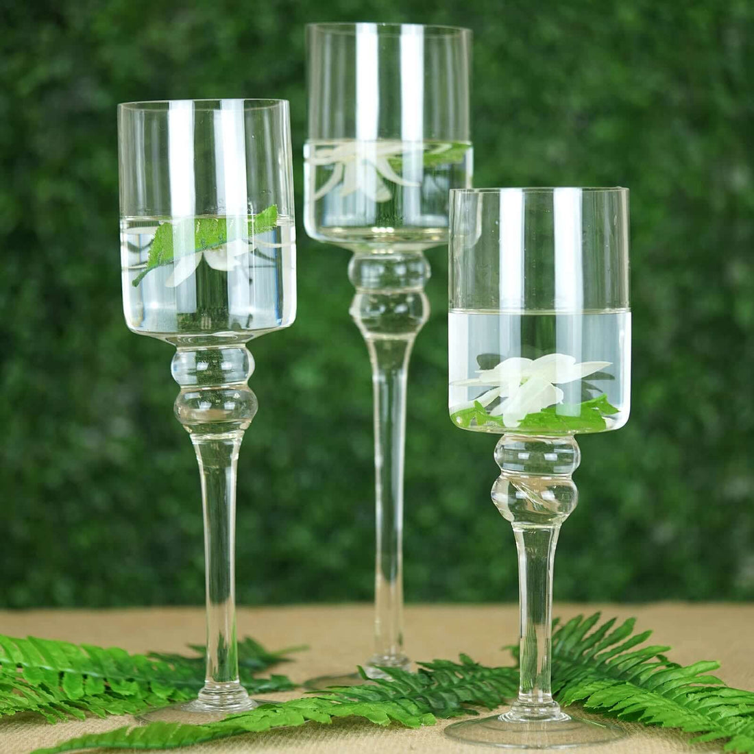 Elegant glass candle holders with flowers and water, set against a green backdrop.
