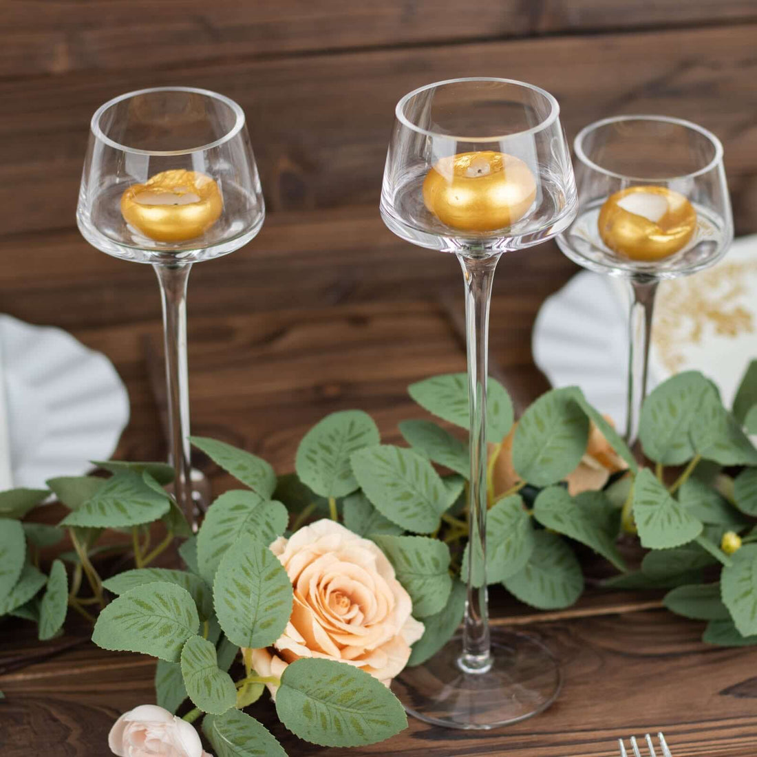 Elegant tall glass candle holders with gold accents and roses on a rustic wooden table.