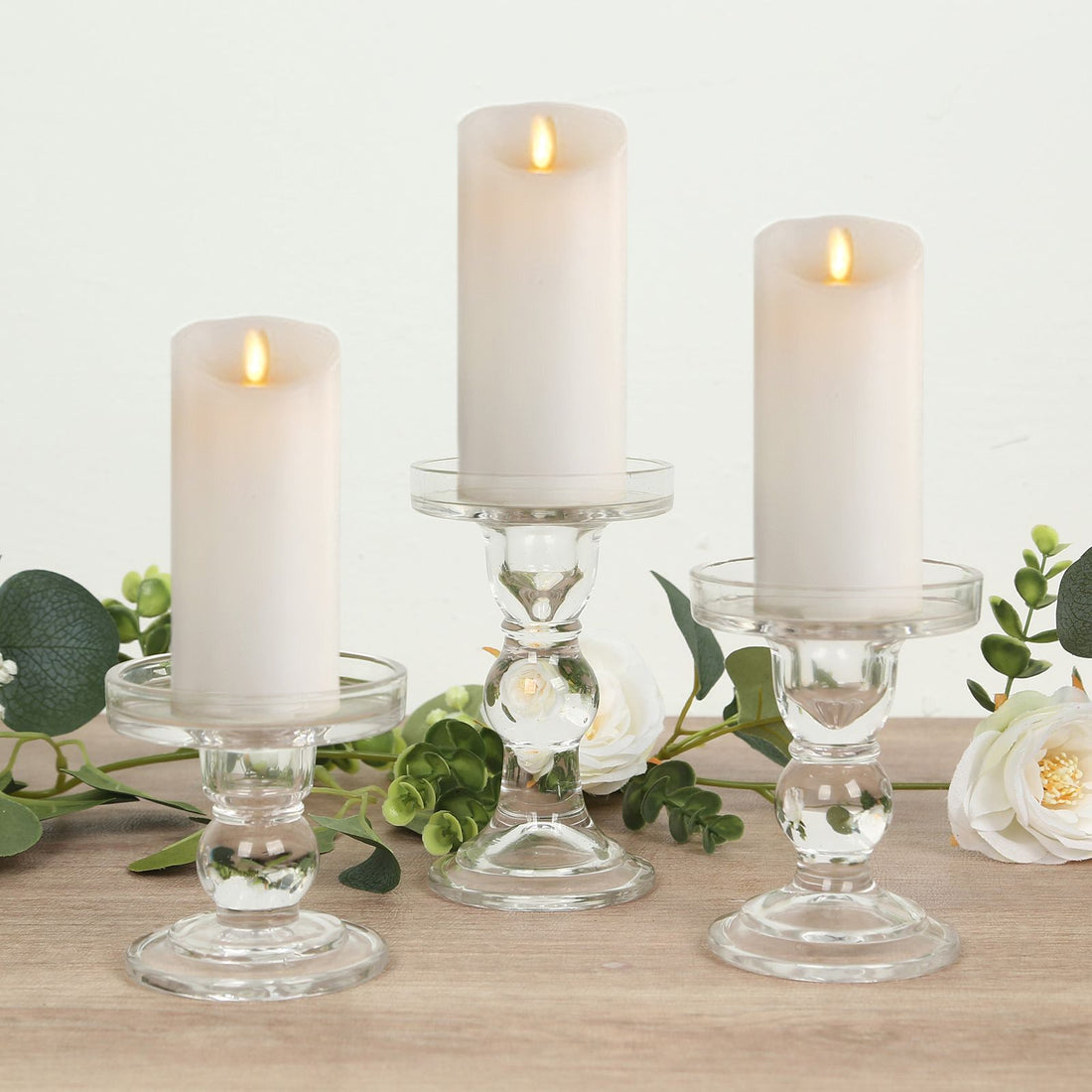 Elegant glass candle holders with white candles, surrounded by greenery.