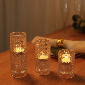 Three decorative glass candle holders with lit candles on a wooden table.
