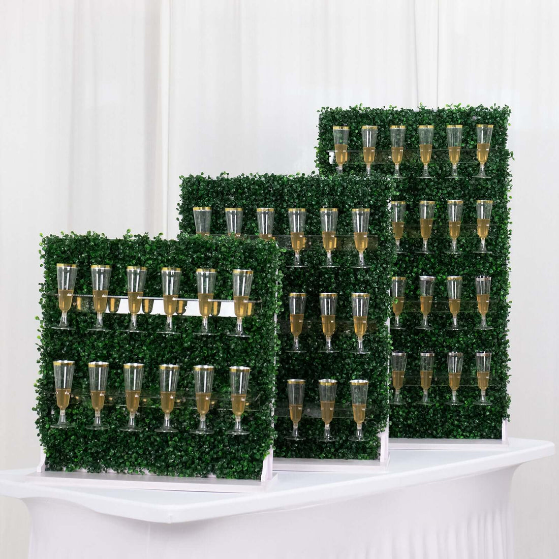 Champagne wall display with glasses filled with bubbly on greenery backdrop.
