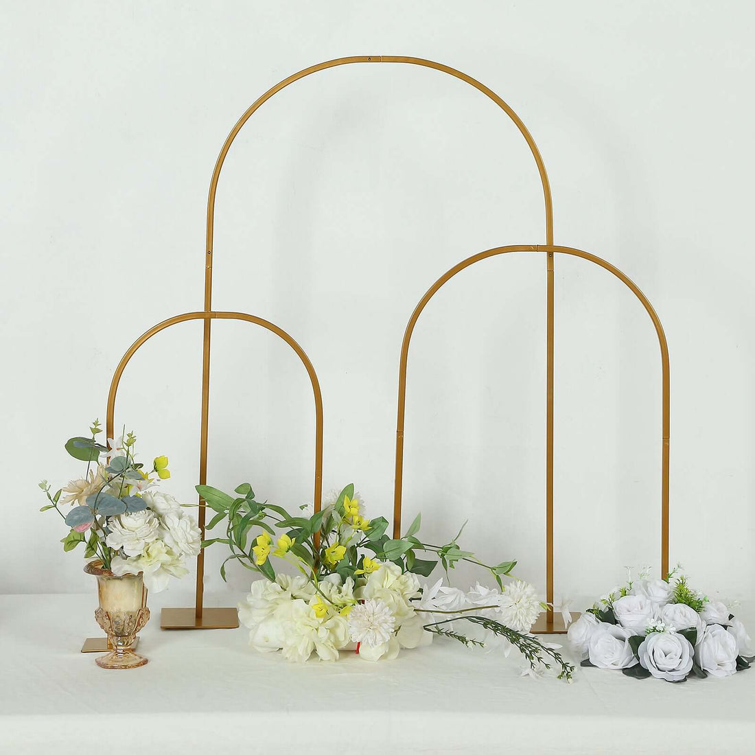 Gold arch backdrop stand with flowers arranged on a table.