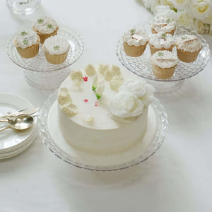 Elegant white cake with floral decoration and cupcakes on clear stands.
